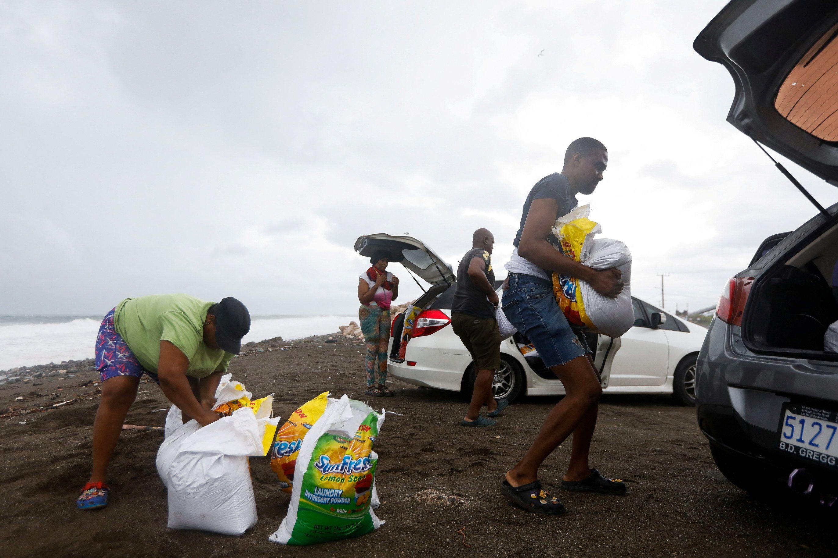 Varias personas cargan costales de arena a sus vehículos en una playa de Jamaica 