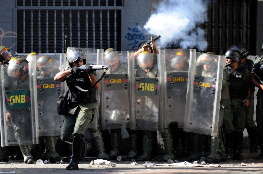 Miembros de la GNB se protegen detrás de sus escudos mientras disparan sus armas.