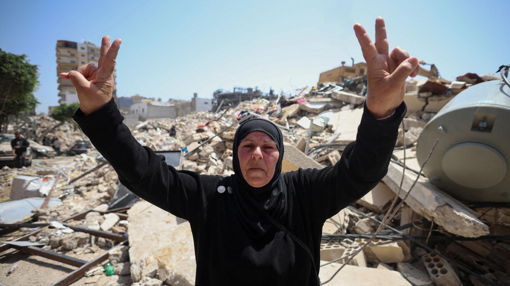 Una mujer libanesa de mediana edad, con vestidura islámica negra, hace la señal de la paz con dos manos en alto, frente a los escombros causados por los ataques israelíes en la ciudad de Tiro