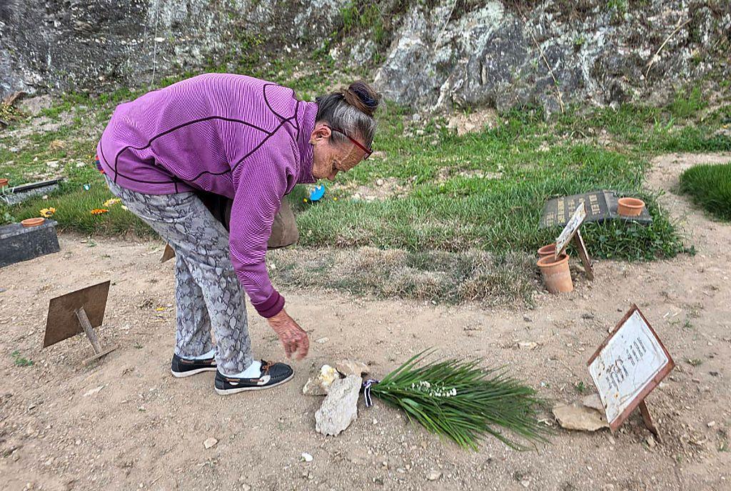 Carmen Nava deposita flores en la tumba de su hijo. Es un suelo de tierra donde la única identificación es una placa metálica con lo que parece un papel encima donde pone el nombre de su hijo. Ella está agachada, tras depositar un ramo que ha dejado pillado con varias piedras. Es una mujer visiblemente mayor, encorvada. 
