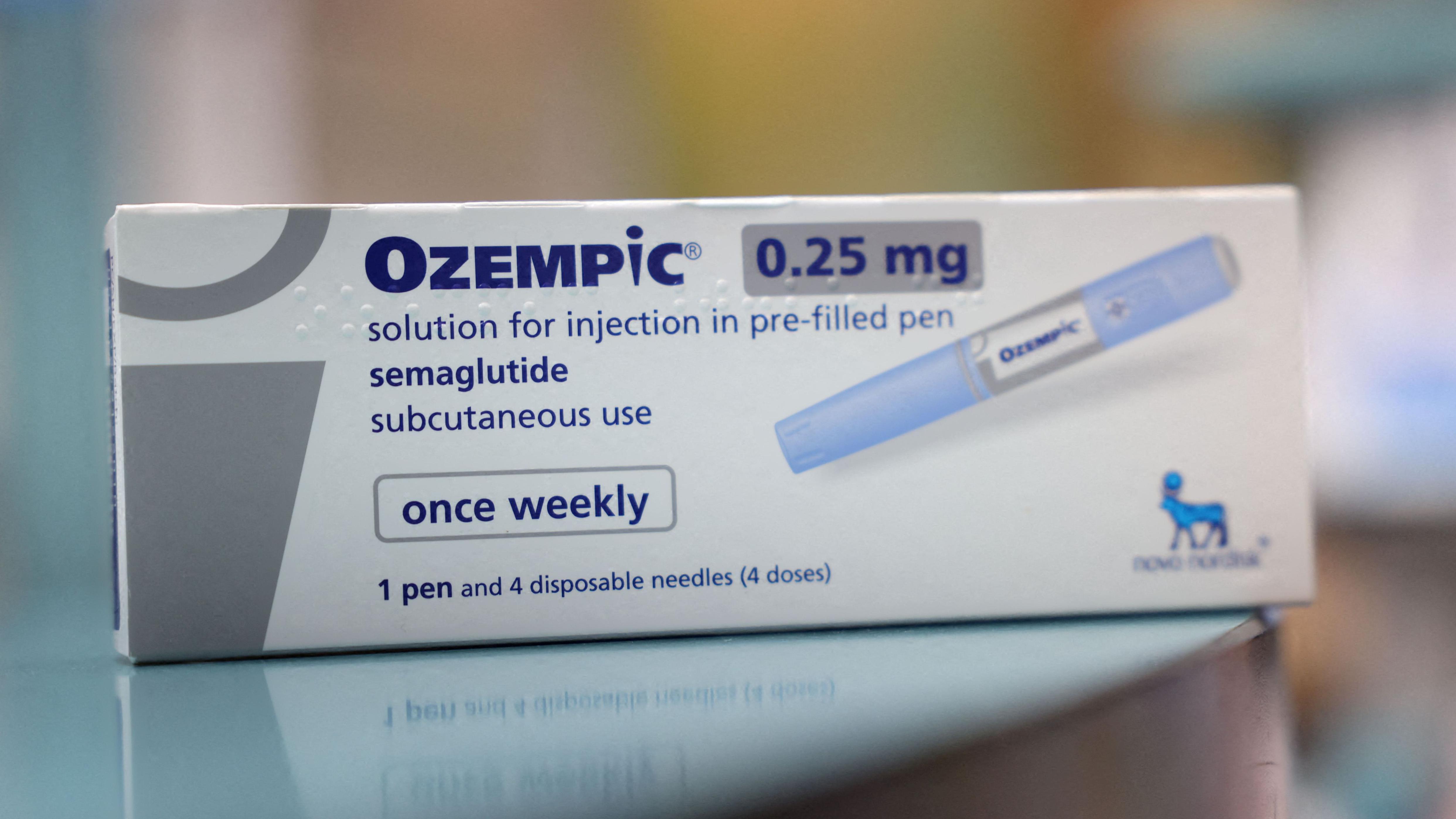 A imagem mostra uma caixa do medicamento Ozempic 0,25 mg, com destaque para a informa&ccedil;&atilde;o de que se trata de uma solu&ccedil;&atilde;o injet&aacute;vel de semaglutida em caneta pr&eacute;-preenchida, indicada para uso subcut&acirc;neo uma vez por semana; a embalagem, predominantemente branca com detalhes em azul, exibe a ilustra&ccedil;&atilde;o da caneta aplicadora, a indica&ccedil;&atilde;o de que cont&eacute;m uma caneta e quatro agulhas descart&aacute;veis (quatro doses) e o logotipo da fabricante Novo Nordisk no canto inferior direito, apoiada sobre uma superf&iacute;cie lisa com o fundo desfocado.