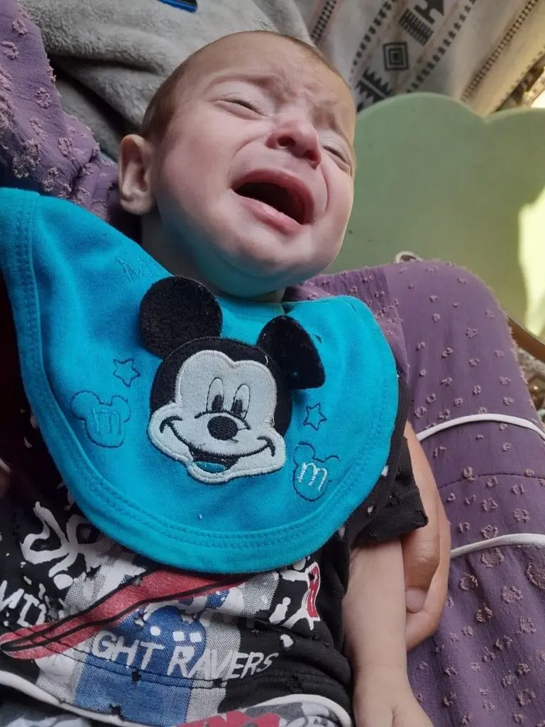 الطفل نضال لون بشرته أبيض شعره خفيف، قبل وفاته بأسبوع يرتدي ملابس أطفال ملونة يطغى عليها اللون الأزرق. يبكي ويبدو أنه في حضن والدته التي لا تظهر ملامحها في الصورة.