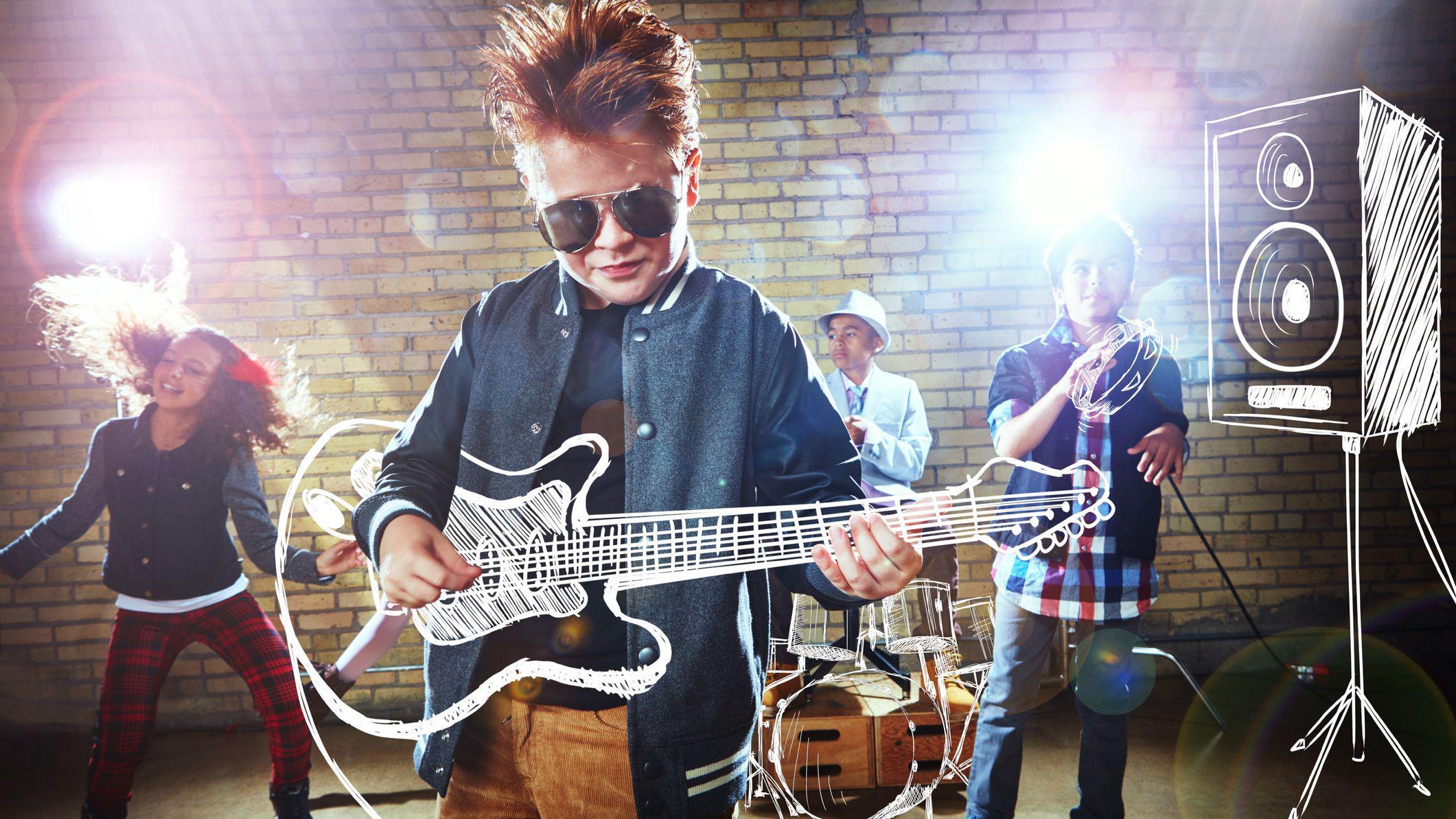 طفل يرتدي نظارة شمسية، يقف في مقدمة فرقة موسيقة تقودها مجموعة أطفال ويعزف على آلة الغيتار.