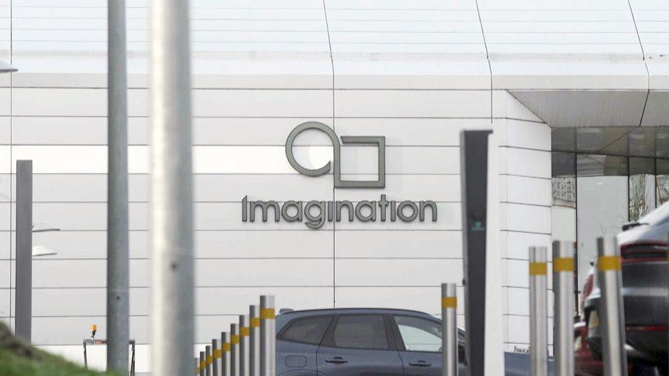 現代白色建築外觀，牆上印有 Imagination Technologies 標誌，圖案由圓形與方形組成，位於「Imagination」字樣上方。前景排列多個防撞柱，入口附近可見停放的車輛。