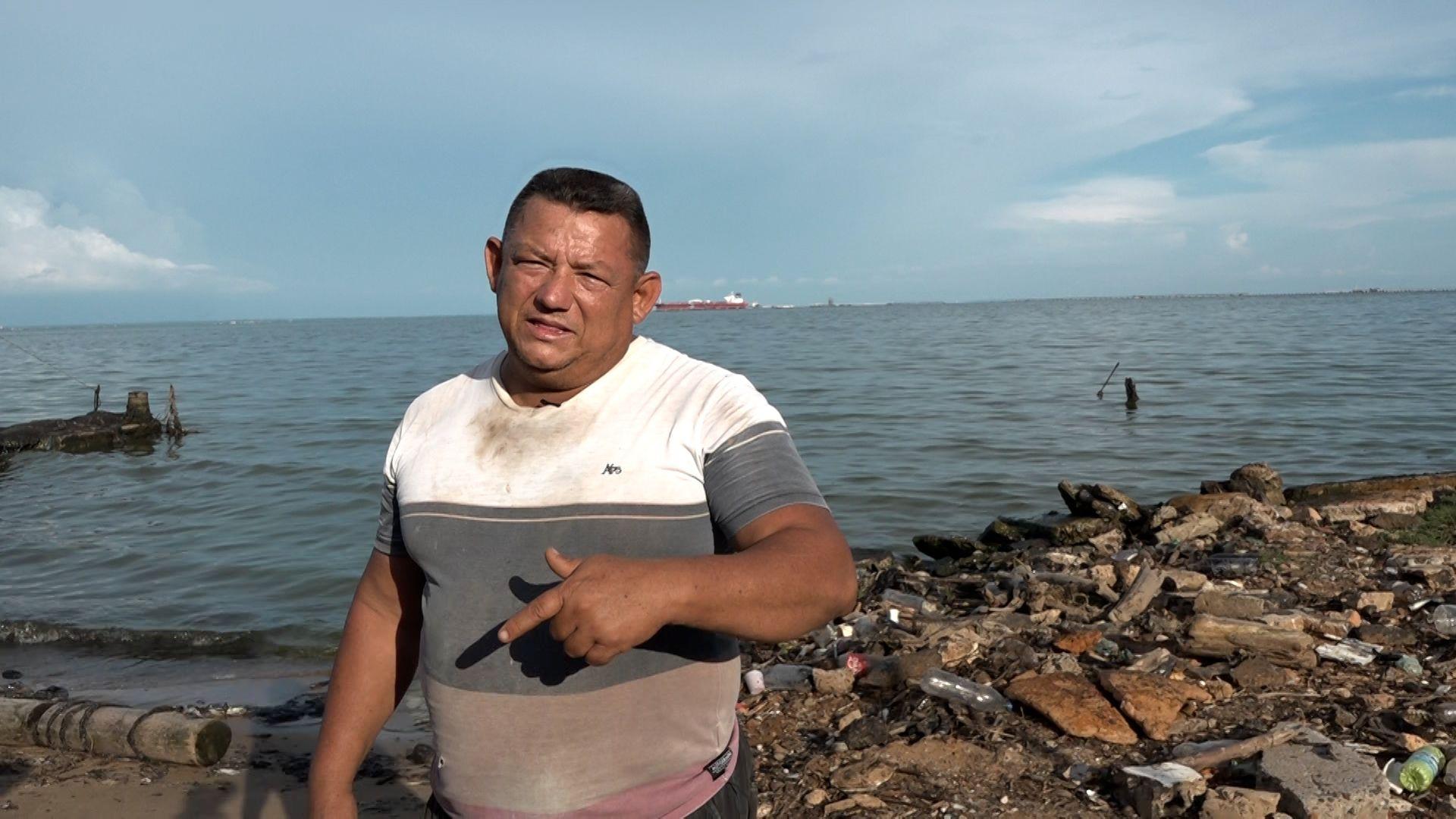 José Luzardo viste una camiseta blanca, gris, marrón y roja con una gran mancha en la parte superior de su pecho. Detrás de él se ve el mar.