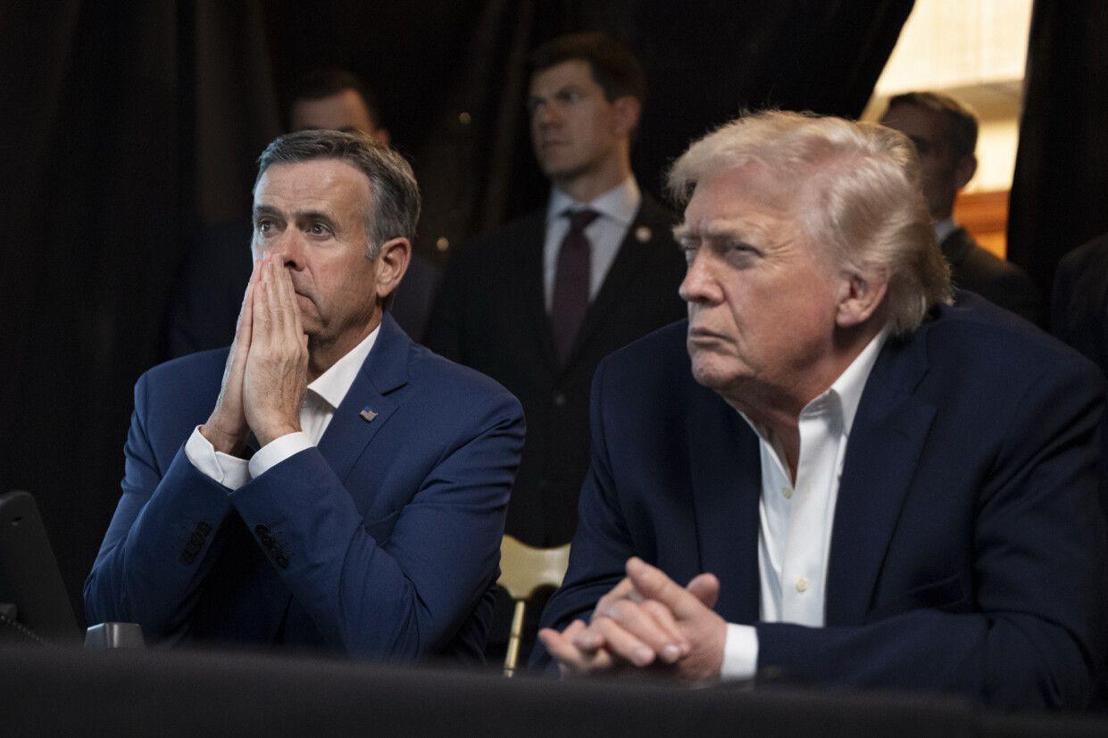 Ratcliffe con las dos manos juntas frente a su rostro, y Trump con cara seria y las manos sobre la mesa, una encima de la otra.