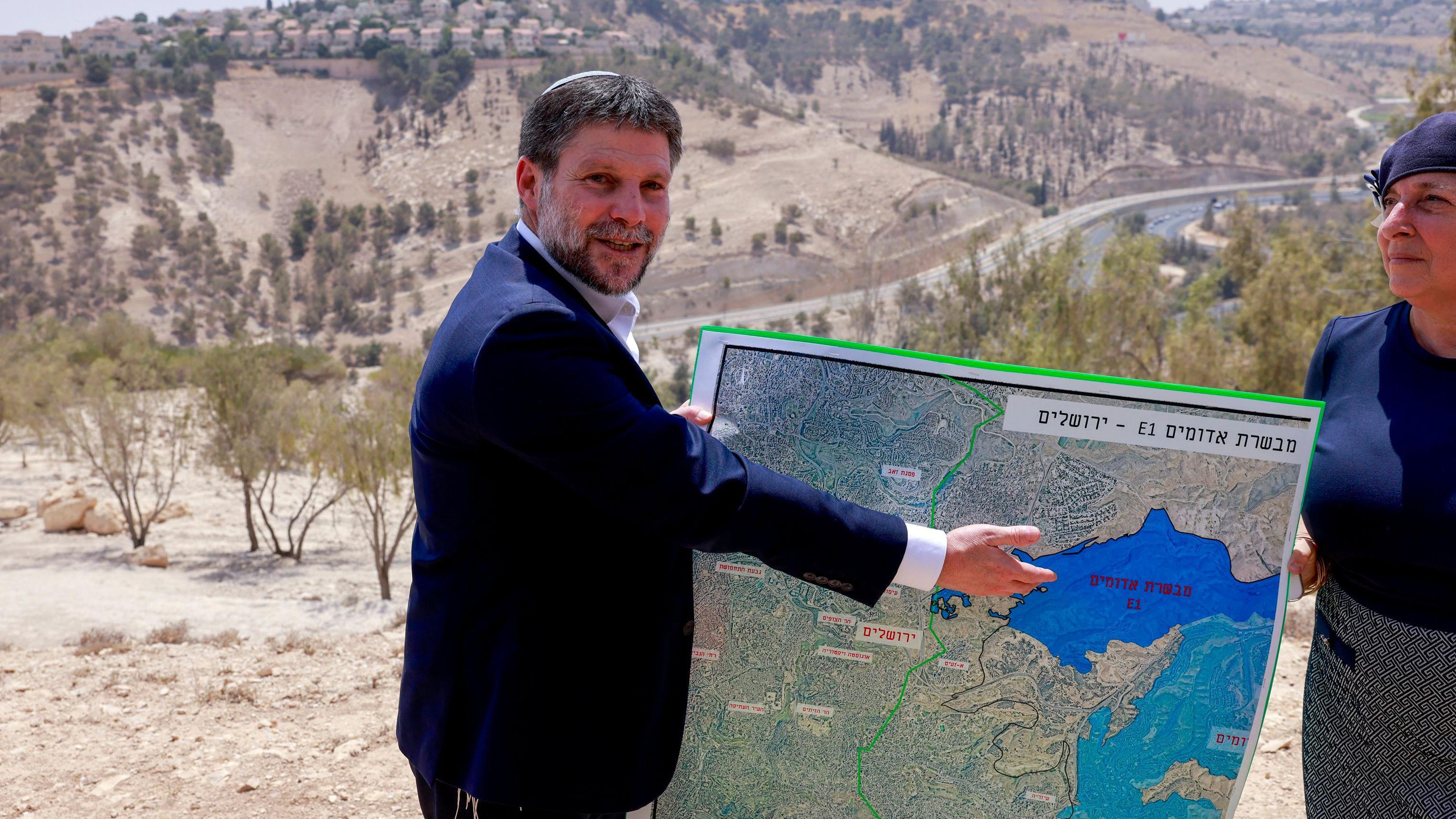 يعرض وزير المالية الإسرائيلي اليميني المتطرف، بتسلئيل سموتريتش، خريطةً لمنطقة قرب مستوطنة معاليه أدوميم، وهي ممرٌّ أرضيٌّ يُعرف باسم E1، يقع خارج القدس في الضفة الغربية المحتلة، في 14 أغسطس/آب 2025، بعد مؤتمر صحفي عُقد في الموقع. 