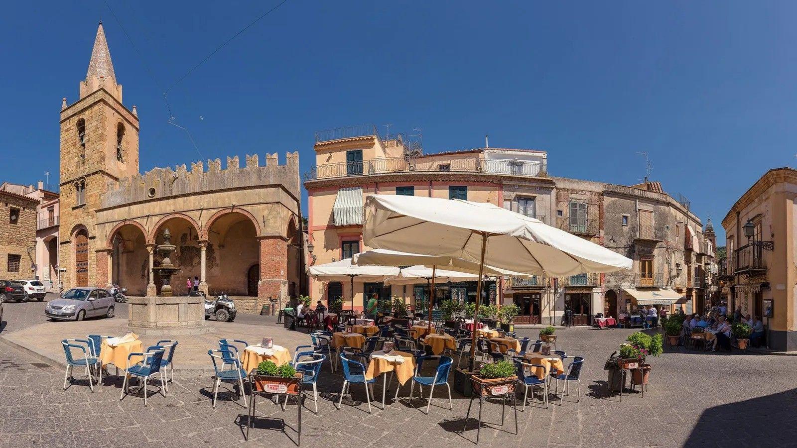 Una plaza con sillas, mesas y sombrillas.