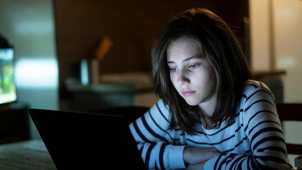 شابة تنظر بجدية إلى شاشة كمبيوتر في غرفة مظلمة