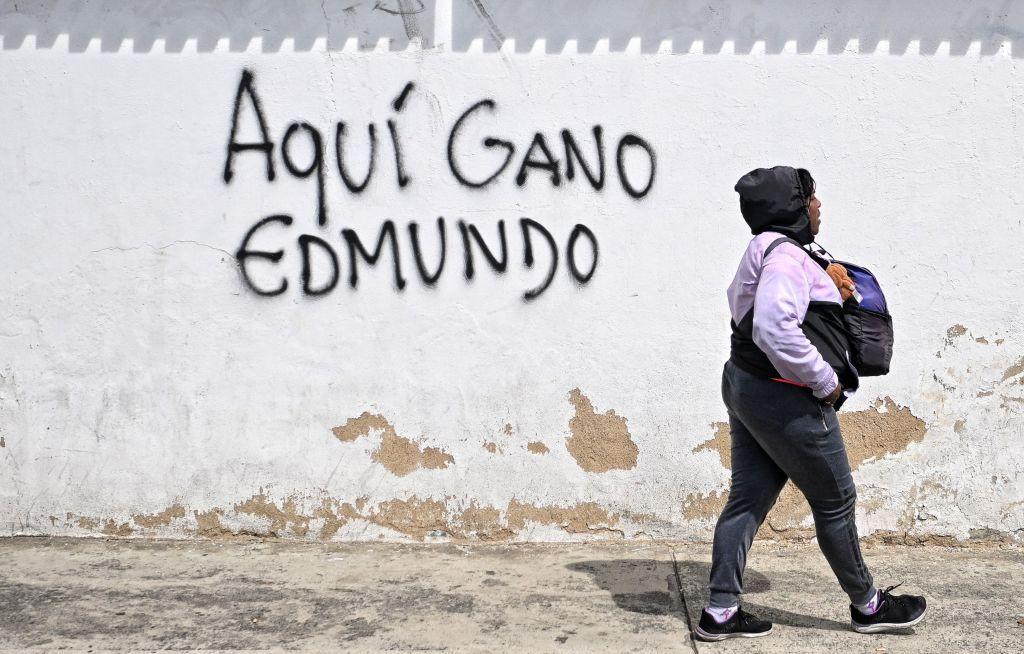 Una mujer camina por una calle donde hay un grafiti que dice "aquí ganó Edmundo".