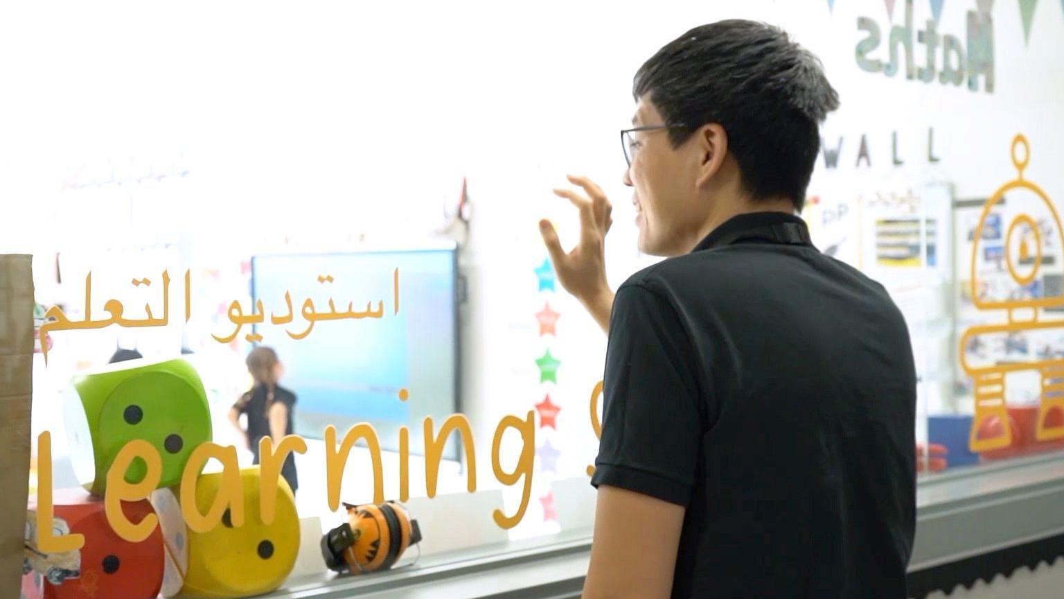 صورة تُظهر والداً يقف خلف زجاج استديو التعليم في إحدى المدارس الخاصة في الإمارات وهو ينظر إلى ابنه داخل الصف ويضع يده على الزجاج.