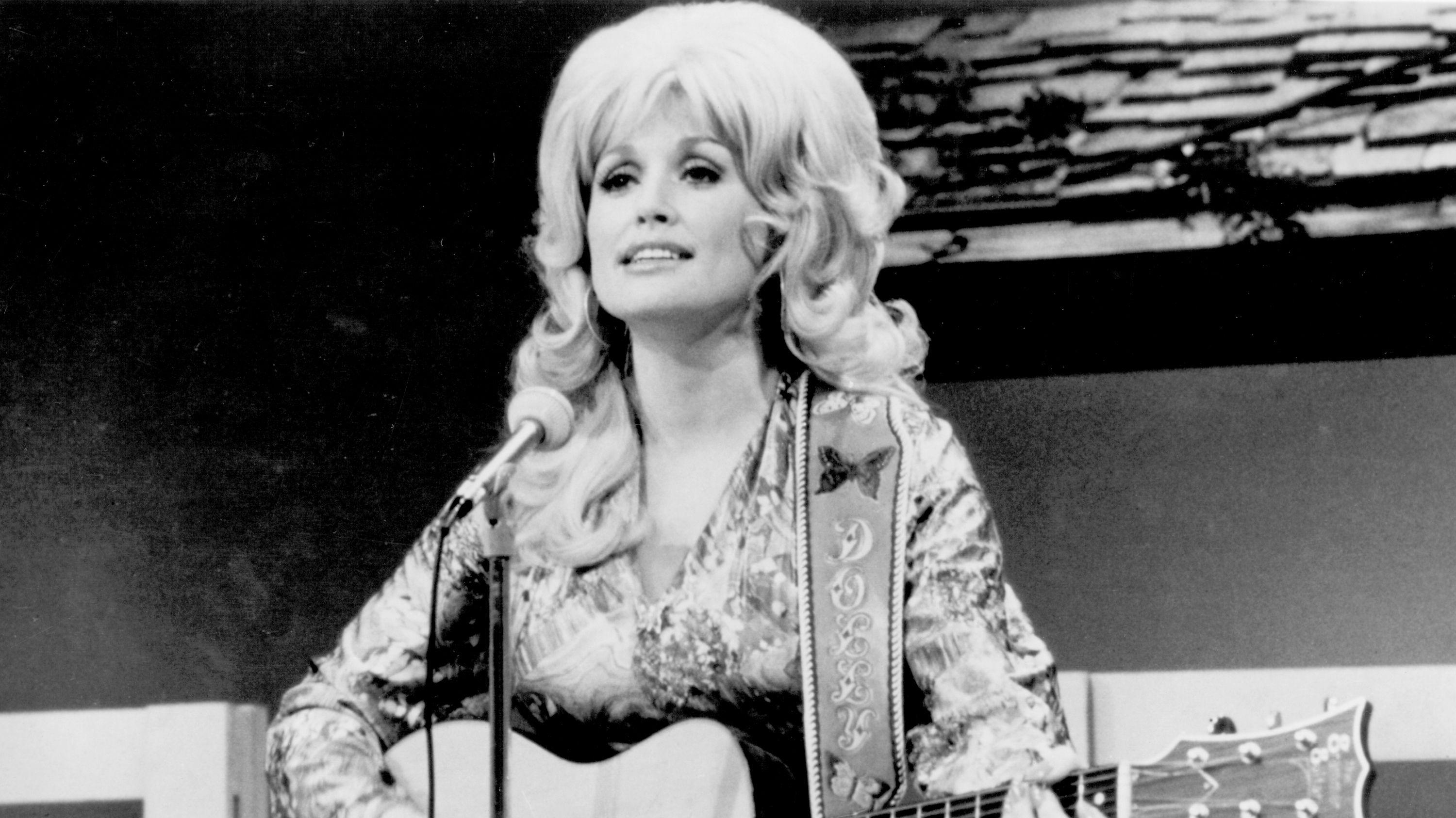 Imagen en blanco y negro de Dolly Parton en el escenario con una guitarra.