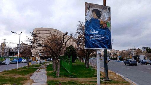 Em primeiro plano, um cartaz ao lado de uma rua exibe uma foto de Helma deitada no hospital, com os olhos fechados. Asas foram desenhadas sobre a imagem, que traz texto em farsi. Ao fundo, h&aacute; um grande pr&eacute;dio de escrit&oacute;rios