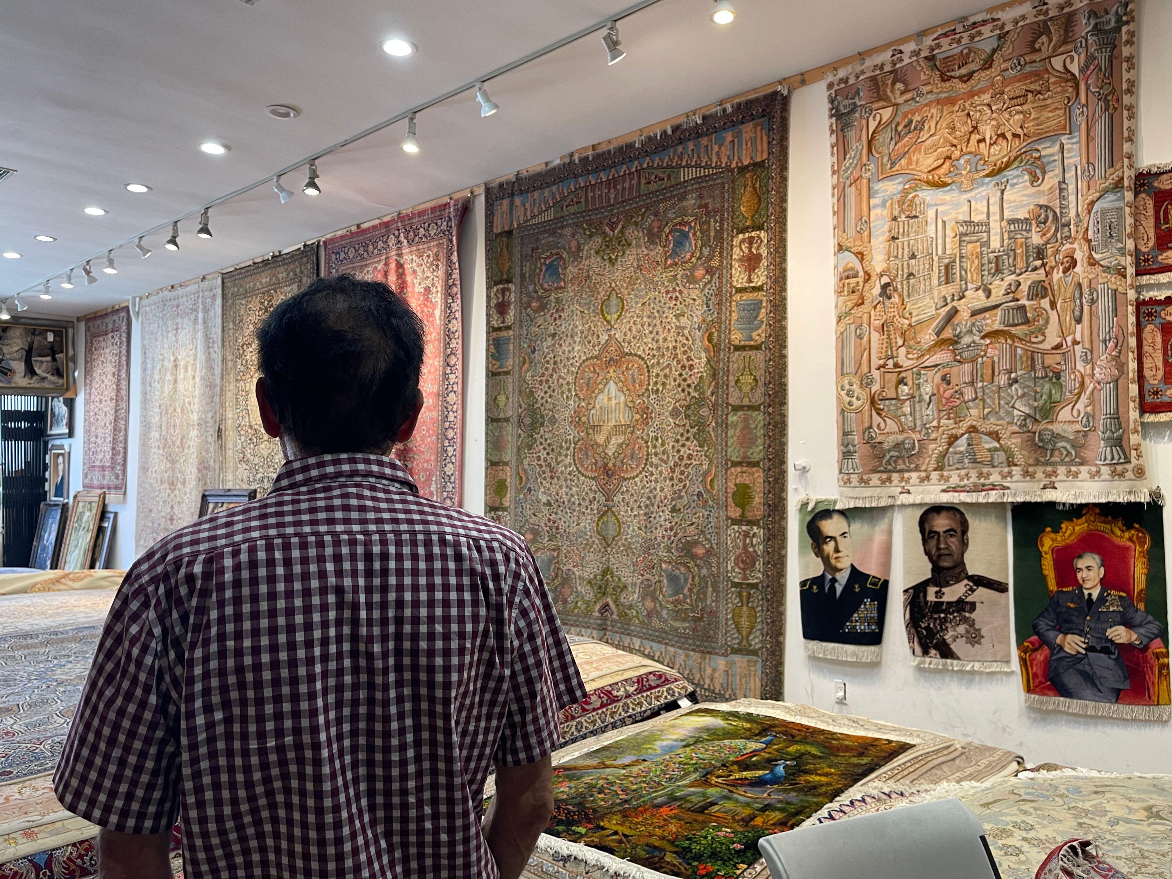 Eric Saddith de espaldas en su tienda alfombras de Teherángeles, con alfombras colgadas de las paredes y tapices con el retrato del último sha de Irán, Mohamed Reza Pahlavi, el 15 de junio de 2026. (Foto: Leire Ventas)