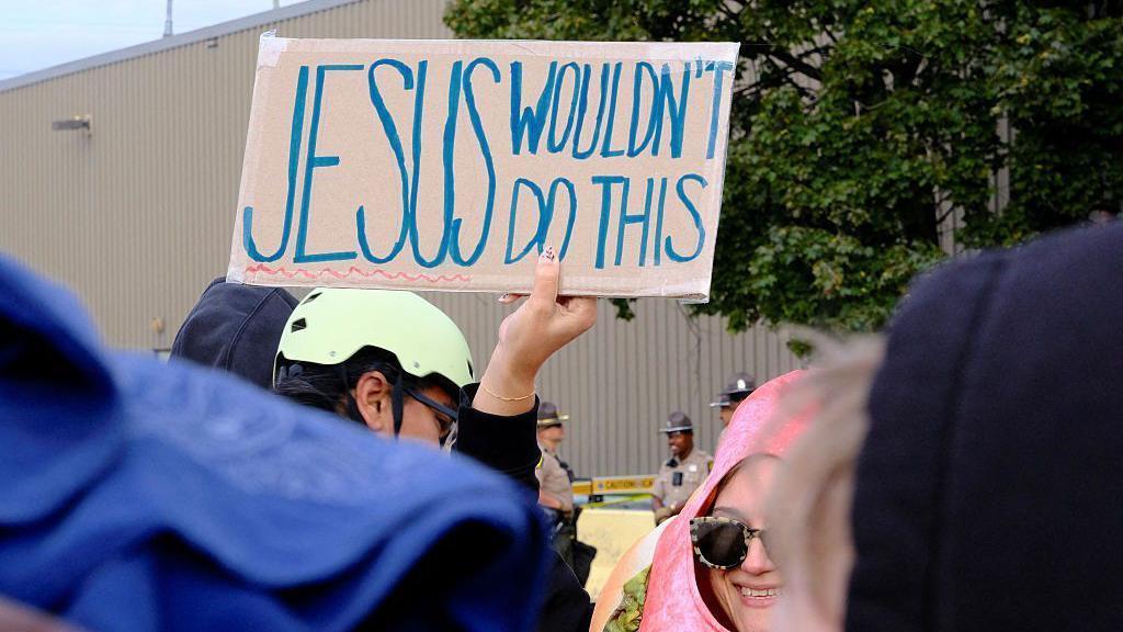 كاثوليك يتظاهرون أمام مركز للمهاجرين ويرفعون لافتة مكتوب عليها بخط اليد "المسيح لم يكن ليفعل هذا"