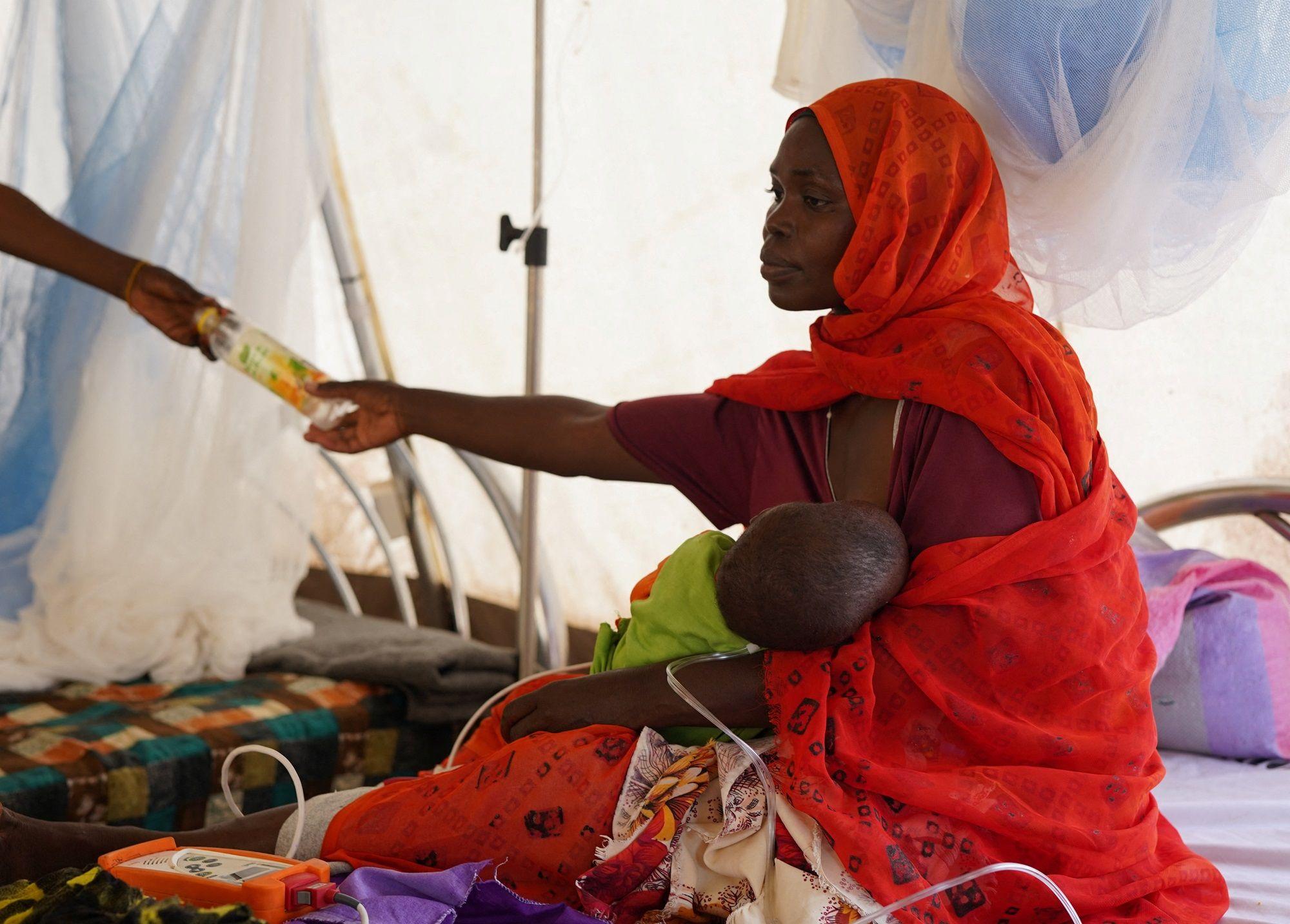 امرأة سودانية نازحة مصابة فرت من العنف في الفاشر، تتلقى العلاج أثناء جلوسها مع طفلها في عيادة مؤقتة تديرها منظمة أطباء بلا حدود، وسط اشتباكات مستمرة بين قوات الدعم السريع شبه العسكرية والجيش السوداني، في طويلة، شمال دارفور، السودان، 3 نوفمبر/تشرين الثاني 2025.