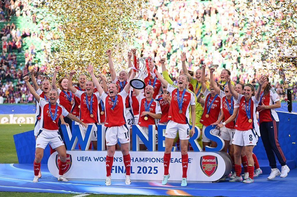 Equipo femenino del Arsenal celebrando el triunfo con sus medallas puestas en la tarima y con papelillos volando