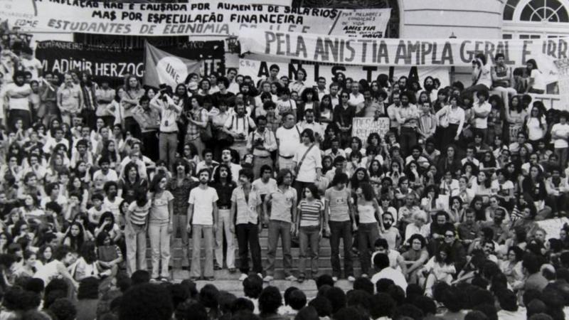 Dezenas de manifestantes em foto em preto e branco; ao fundo, lê-se cartaz que diz: 'Pela anistia ampla, geral e irrestrita'