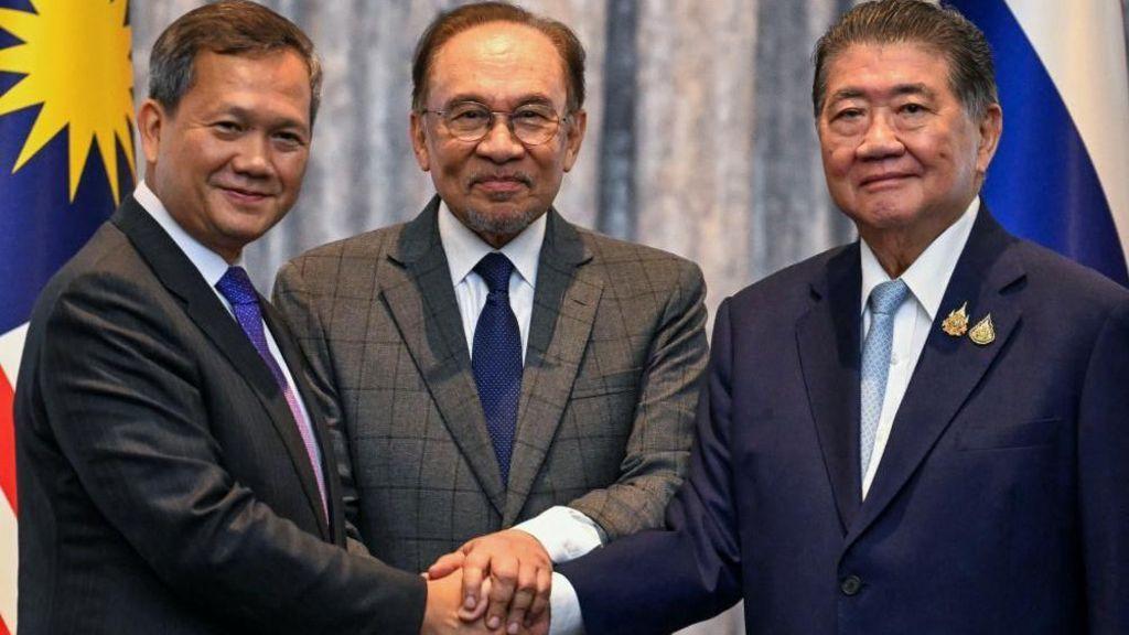 أنور (في الوسط)، ورئيس الوزراء الكمبودي هون مانيت (على اليسار)، ورئيس الوزراء التايلاندي بالنيابة فومثام ويتشاياشاي محادثات السلام في كوالالمبور في يوليو/تموز وجميعهم يرتدون بدلات رسمية ويضعون أيديهم فوق بعضها البعض.