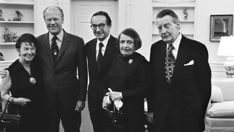 De izquierda a derecha aparecen Rose Goldsmith (madre de Alan Greenspan), el presidente Gerald R. Ford, Alan Greenspan, la escritora Ayn Rand y su esposo Charles Francis «Frank» O'Connor, tras la toma de posesión de Greenspan como presidente del Consejo de Asesores Económicos en el Despacho Oval.