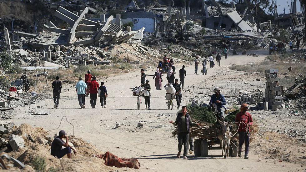 Displaced Palestinians walk past destroyed buildings as they return to their homes in the in al-Zahra area, north of the Nuseirat refugee camp in the central Gaza Strip, on October 14, 2025, a day after a ceasefire came into effect. 