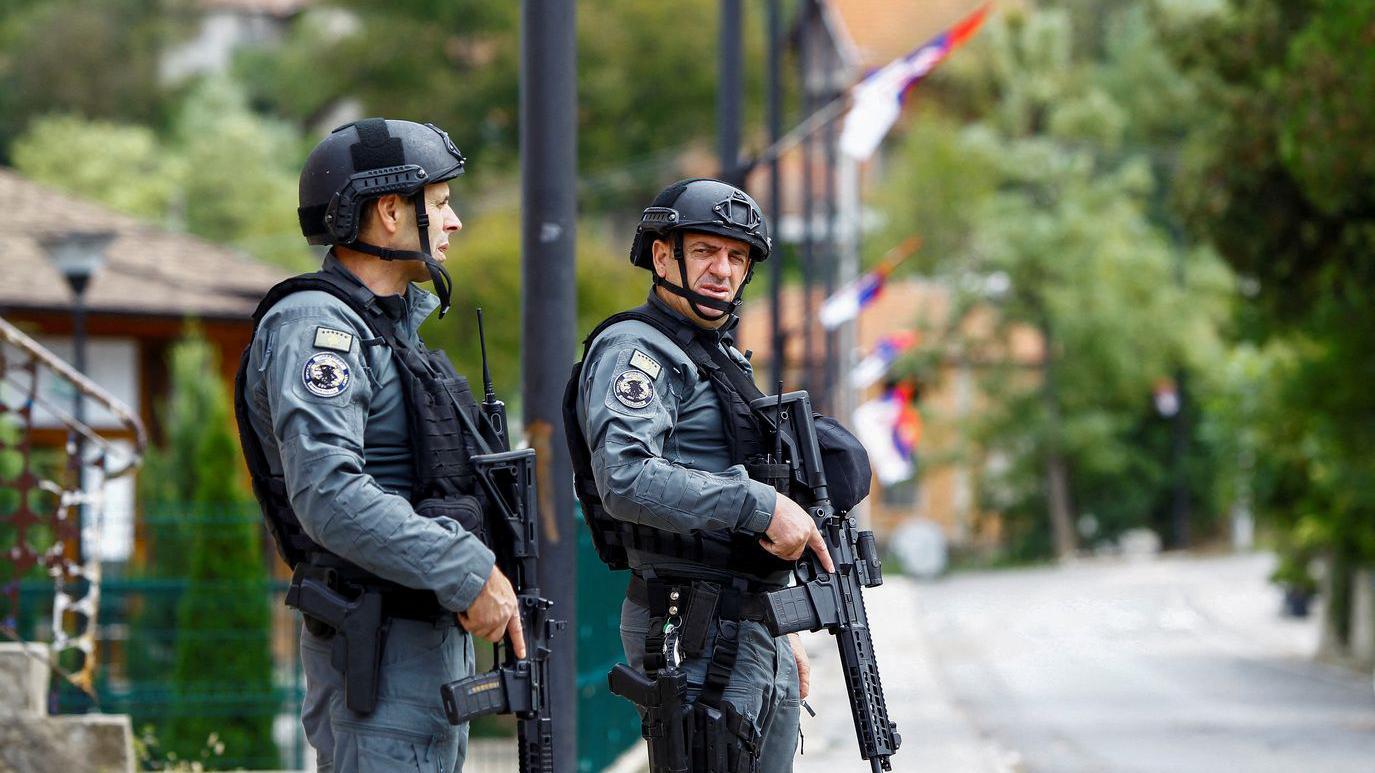 Dva muškarca u policijskoj uniformi sa puškama u rukama, iza njih se naziru srpske zastave