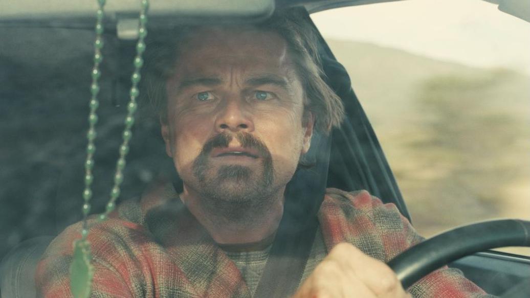 Leonardo Di Caprio conduce un auto y mira por el espejo retrovisor con cara de susto