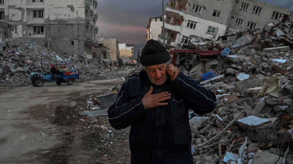 Un hombre habla por teléfono frente a edificios derrumbados, un día después de que un terremoto de magnitud 6,4 azotara la región, en la ciudad costera de Samandag, el 21 de febrero de 2023. 
