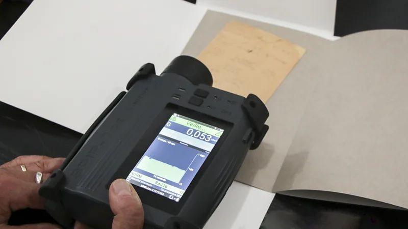 Aparelho preto sendo segurado em cima de um papel com anotações. No visor aparecem alguns números