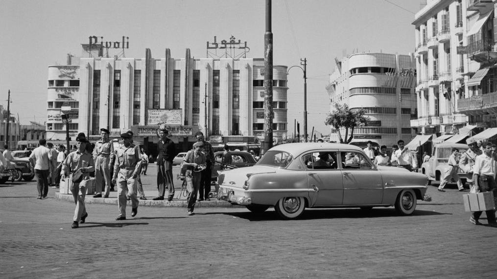 ساحة وسط المدينة في بيروت بالأبيض والأسود، سيارة مرسيدس قديمة، عناصر شرطة سير ومارة وفي الخلف مبنى سينما ريفولي