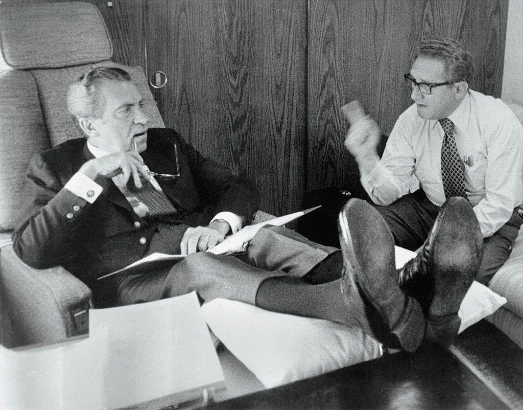 Richard Nixon (izq.), recostado en un asiento del avión presidencial, discutiendo con Henry Kissinger (der.)