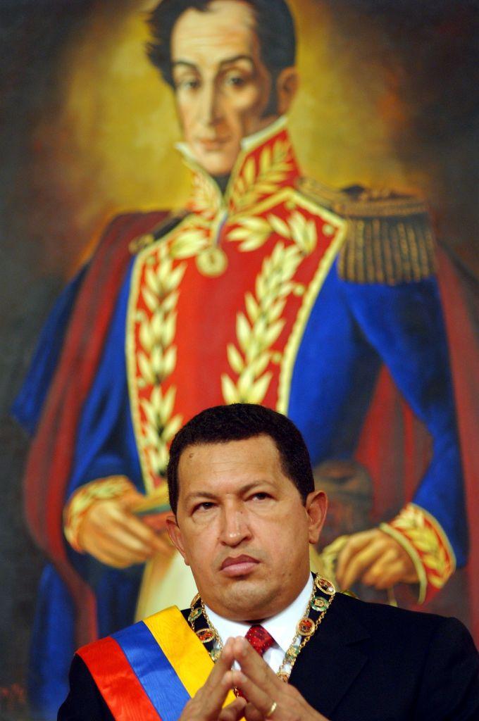 Hugo Chávez con la banda presidencial venezolana sentado delante de un cuadro de Bolívar
