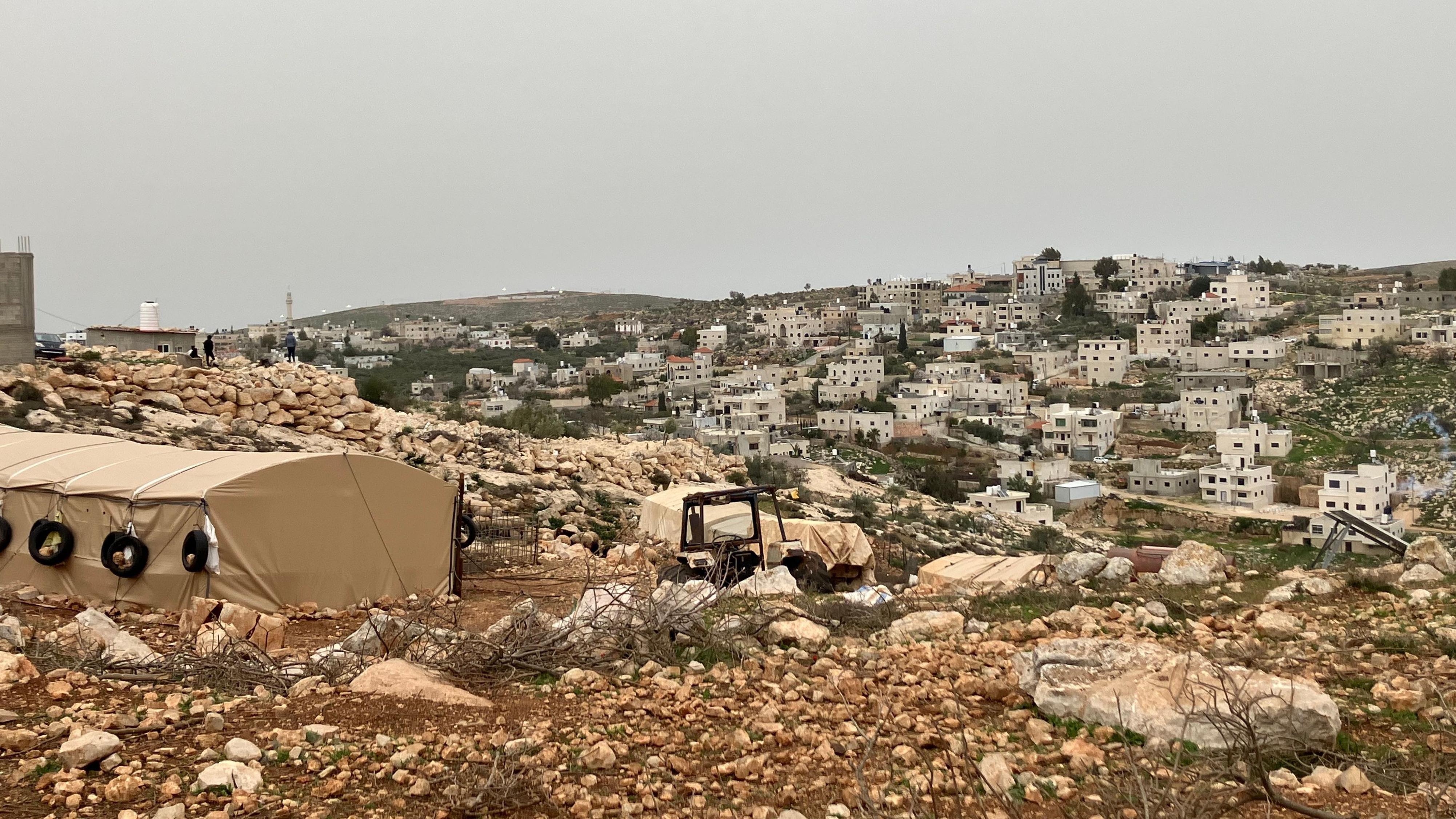 منظر لقرية المغيير، به عشرات المنازل البيضاء المبنية من الطوب الخفيف تنتشر على سفح تل مغطى بصخور بنية وعرة وعشب أخضر.
