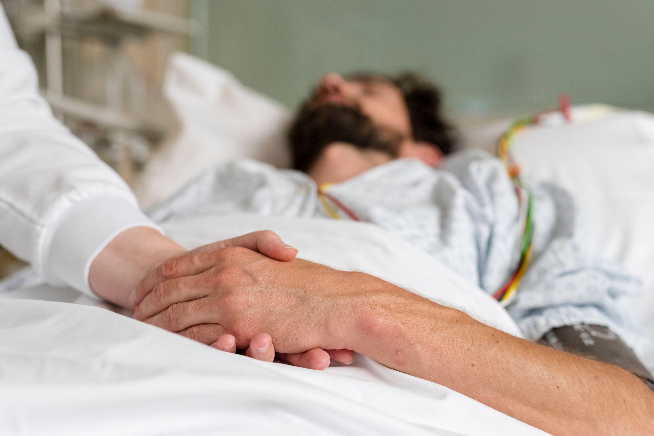 Paciente en cama con la mano entrelazada a la de otra persona
