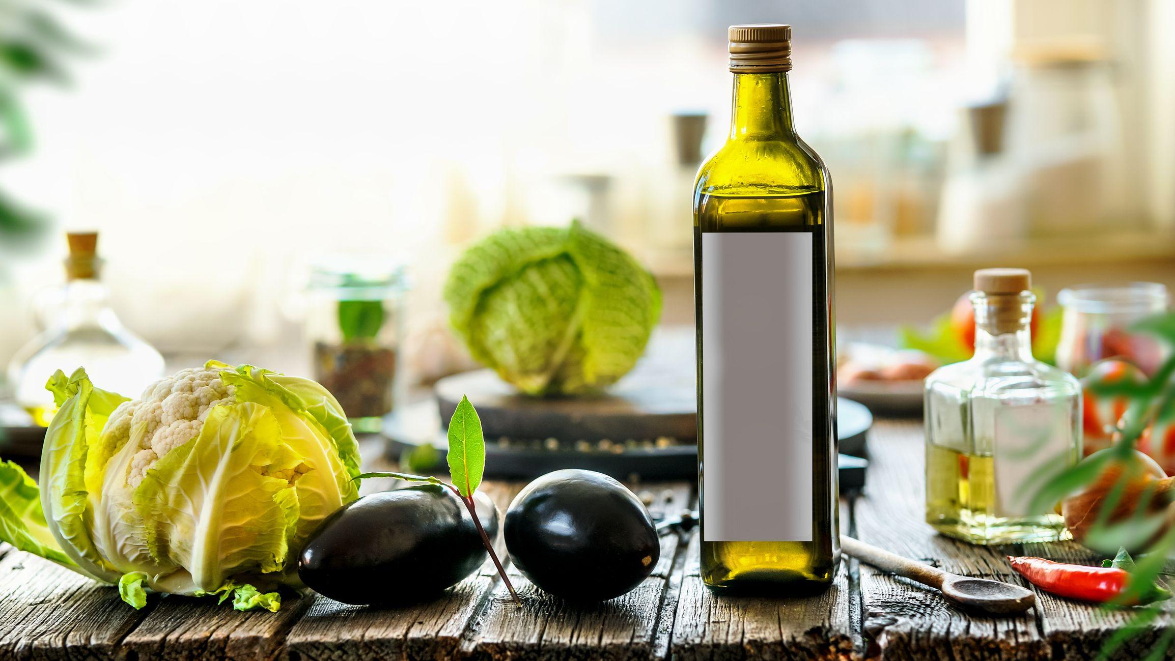 زجاجة تحتوي على زيت الزيتون وبجانبها عدد من الخضراوات