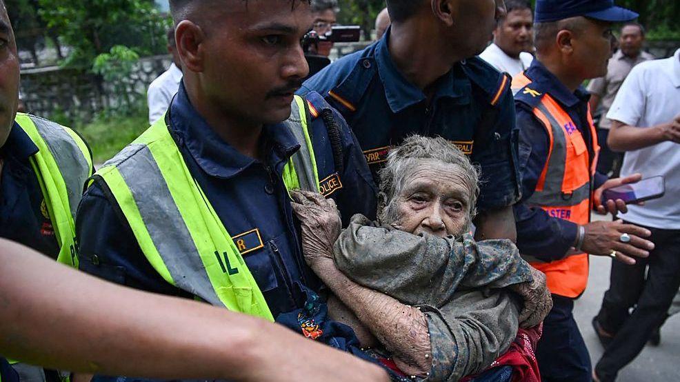 Rescatistas cargan a una anciana cubierta de barro en Nepal.