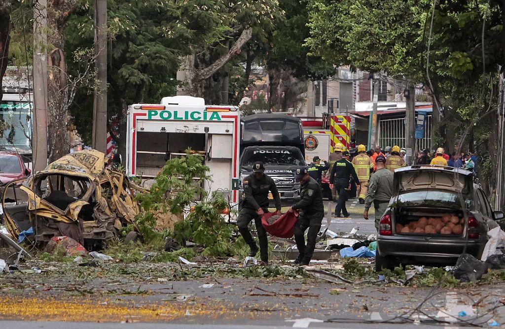 varios policías cargan un cuerpo en unas mantas. caminan entre escombros luego de la explosión en cali, colombia. 