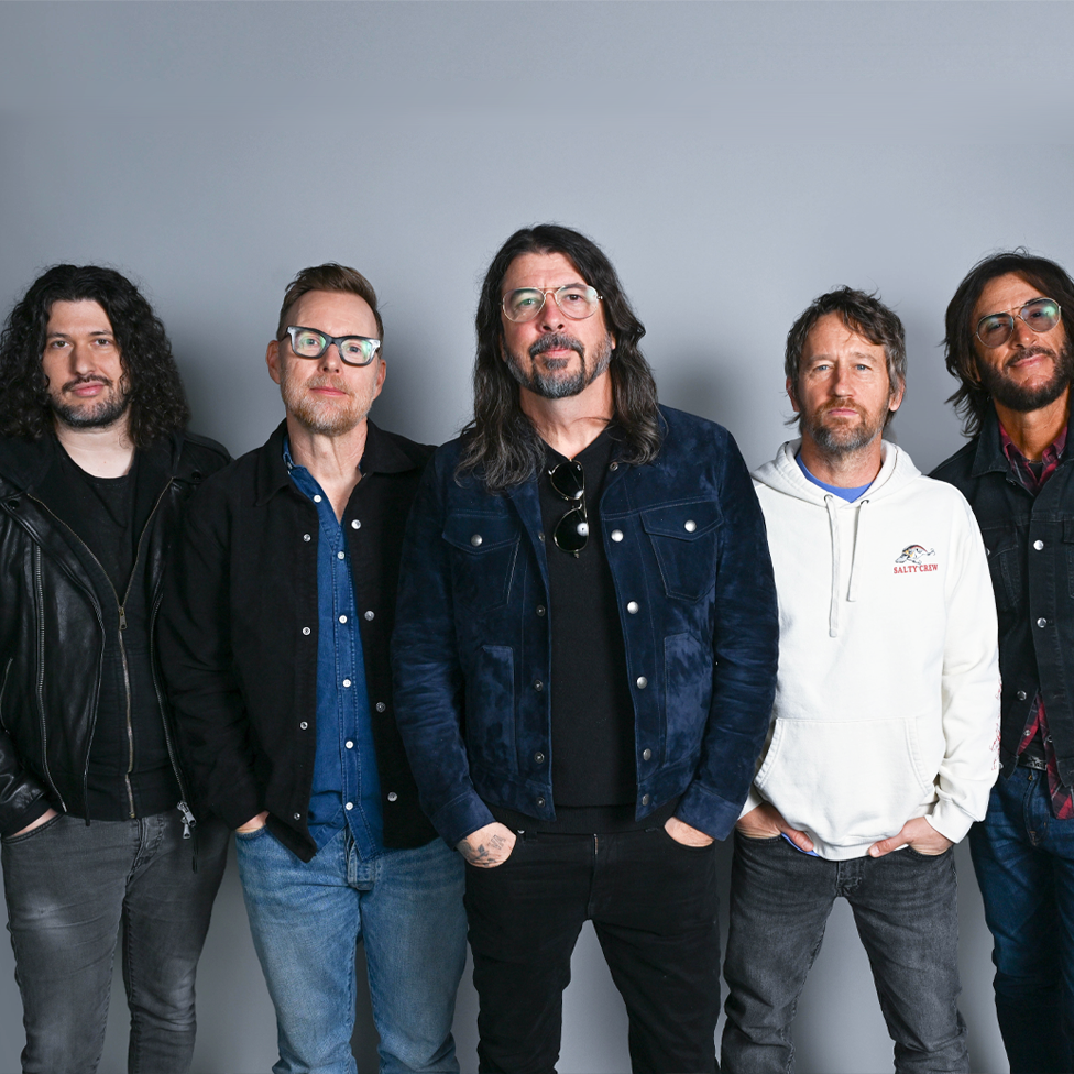 Pet članova benda Fu Fajters stoje jedan pored drugog, gledajući direktno u kameru, sa rukama u džepovima