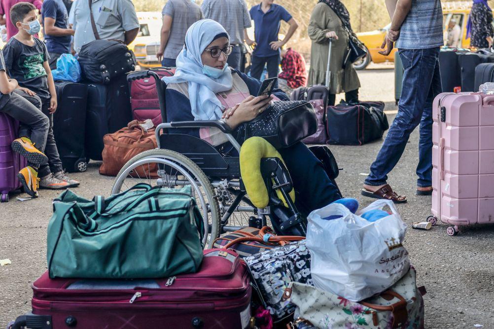 سيدة تجلس على كرسي متحرك وتنتظر دورها في معبر رفح، ترتدي هو طفل خلفها كمامة، يظهر أن الصورة أُخذت وقت انتشار كوفيد 19