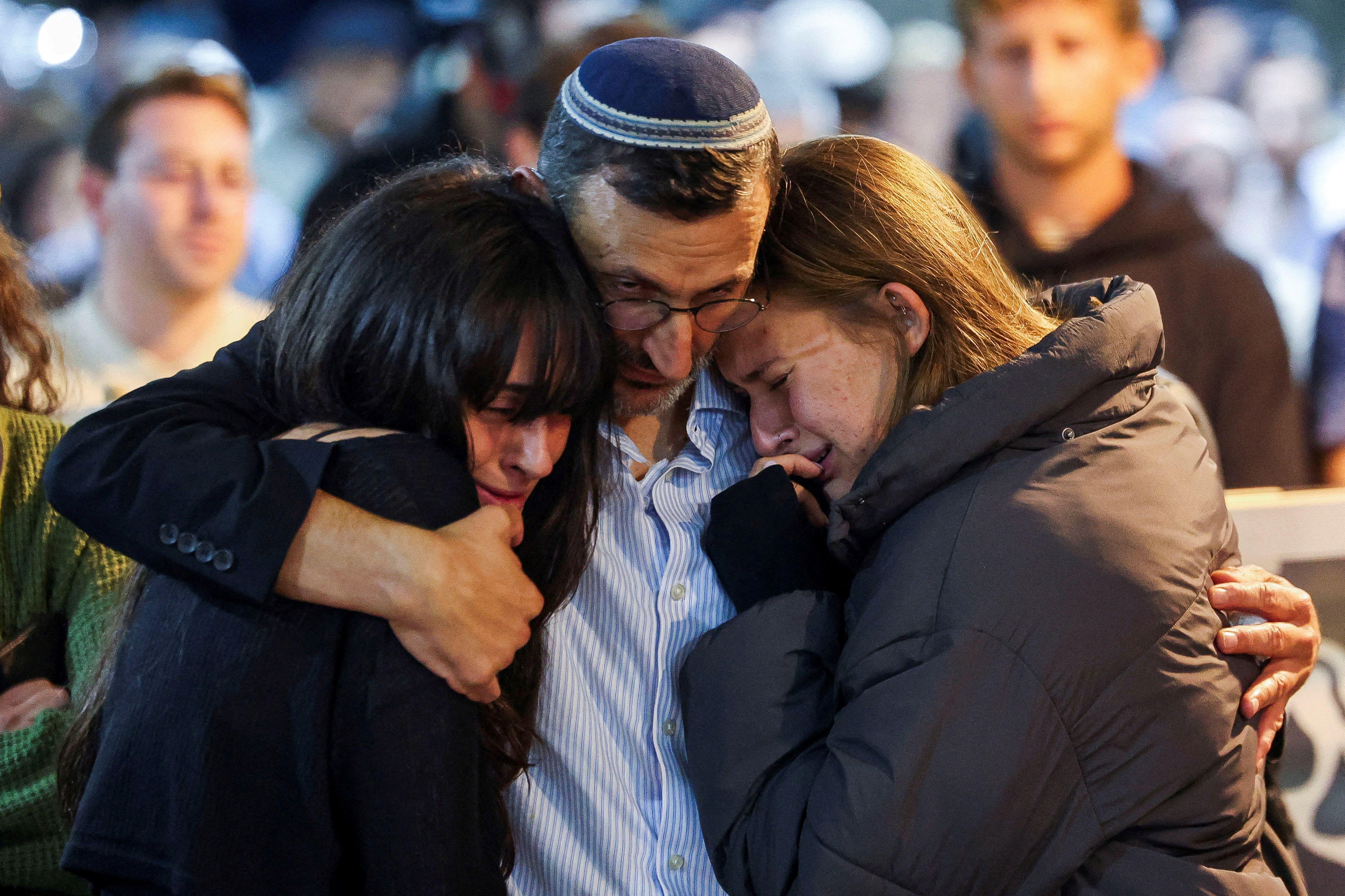 El padre y las dos hermanas de uno de los rehenes israelíes fallecidos se abrazan y lloran.
