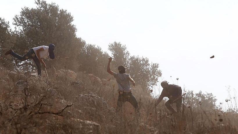 صورة تُظهر مستوطنين ملثمين وهم يحملون العصي ويرشقون الحجارة في بلدة بيتا بمدينة نابلس في الضفة الغربية