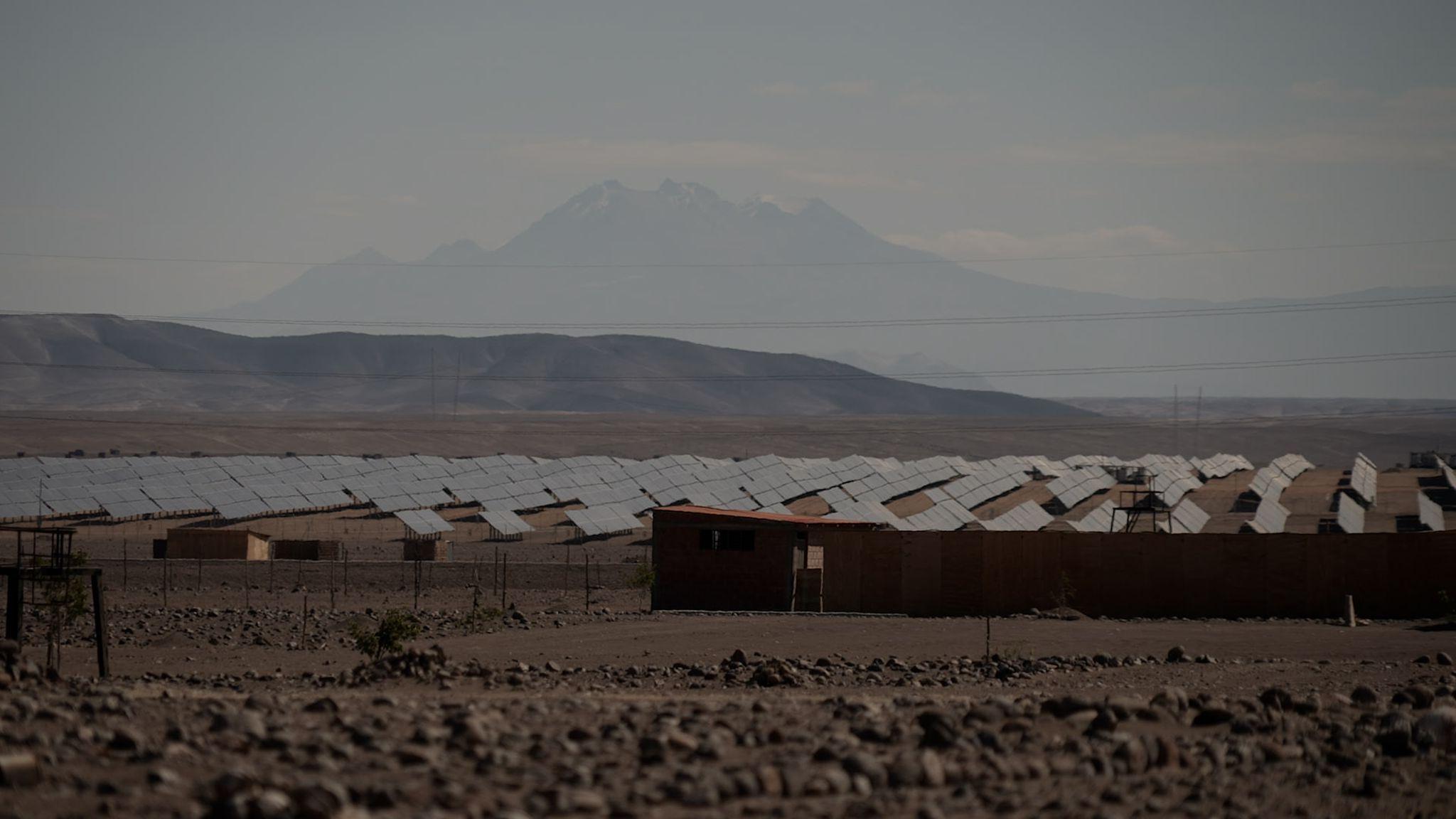 Una casas están enfrente de una larga fila de paneles solares que son parte de la planta solar Rubí.