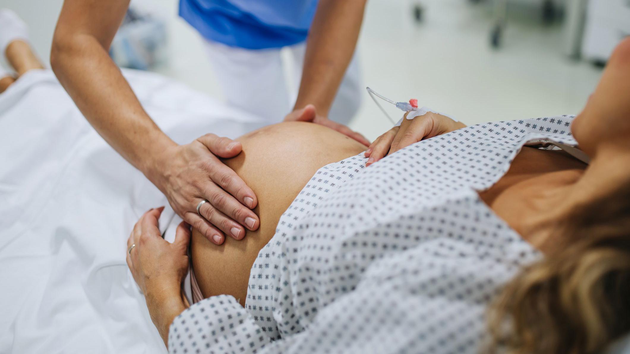 طبيبة نسائية تفحص امرأة حامل في المستشفى، تلمس بطنها، وتفحص وضعية الجنين، ووضعية المقعدة، وحجمه، وحركاته. امرأة في حالة مخاض مستلقية على سرير المستشفى، تتحدث مع طبيبة نسائية في جناح الولادة. 
