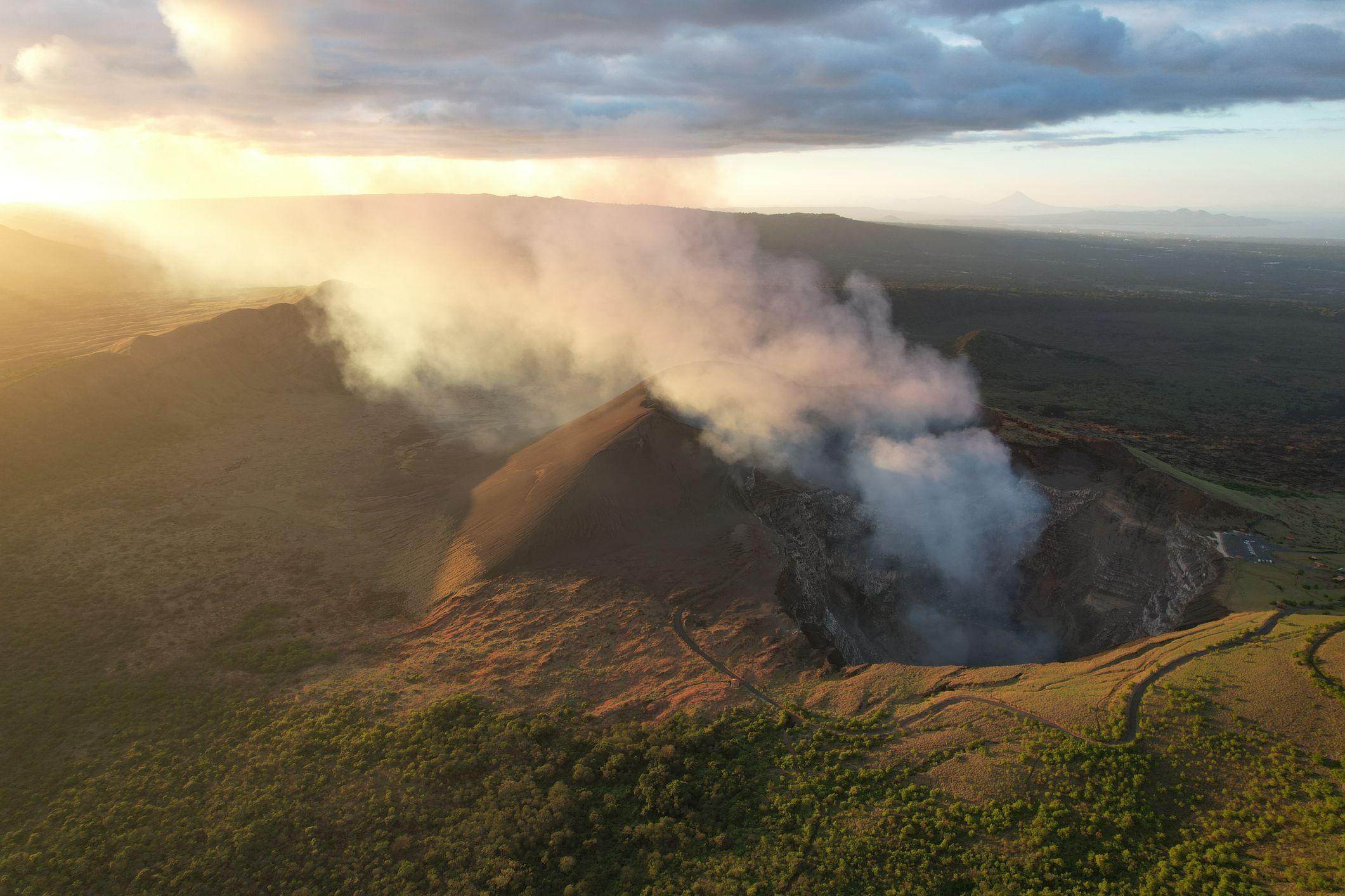 Una foto aérea del volcán Santiago, en Nicaragua. Se ve humo saliendo de su cráter. El humo va ascendiendo hasta que se confunde con las nubes en el cielo al atardecer.