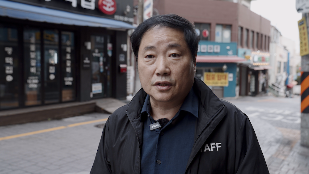 인적이 드문 거리를 배경으로 서 있는 한 남성의 모습을 가까이에서 찍은 사진