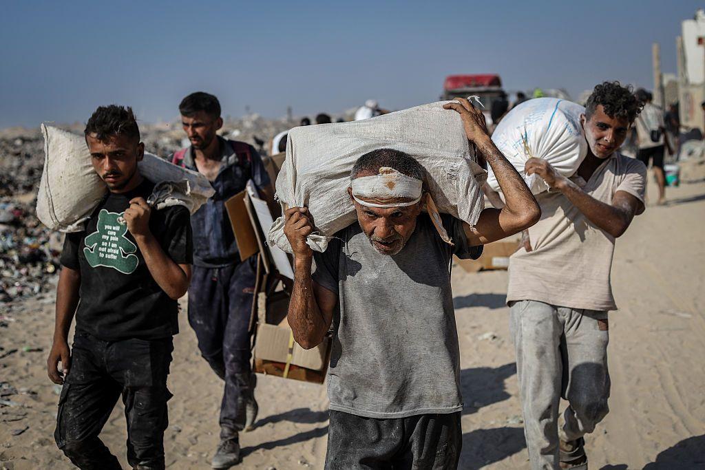 Hombres palestinos cubiertos de polvo cargan sacos en el paso de Zikim. 