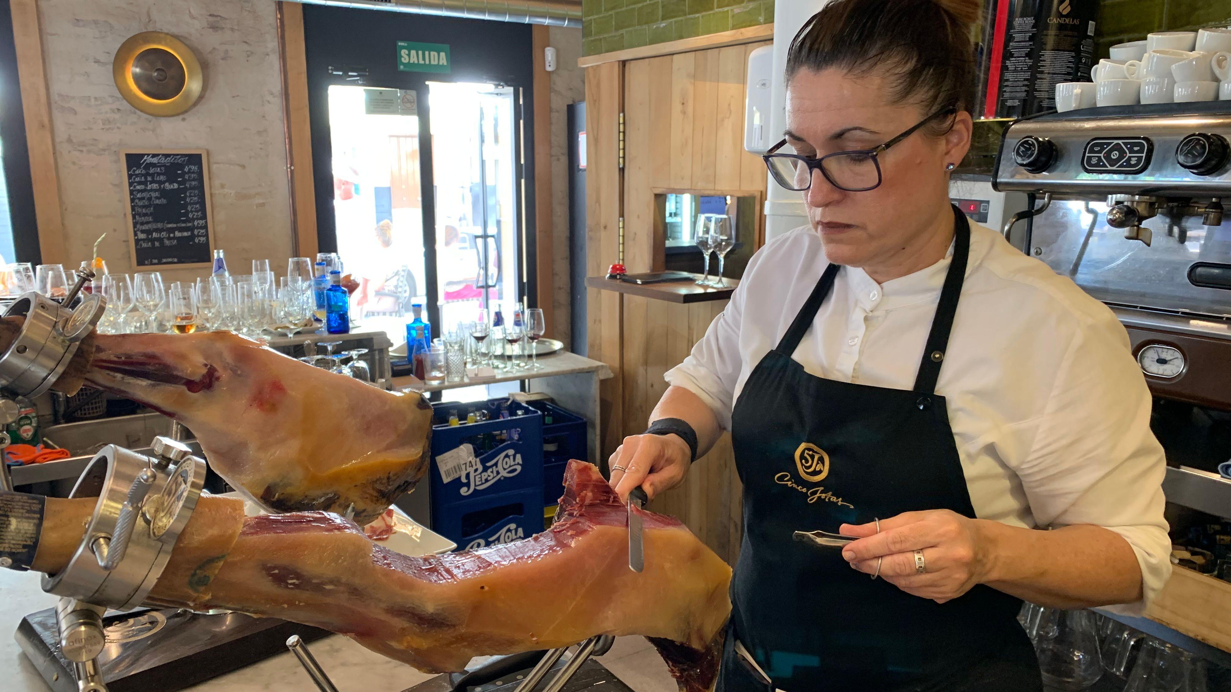 Un bar de Sevilla con una camarera cortando jamón.