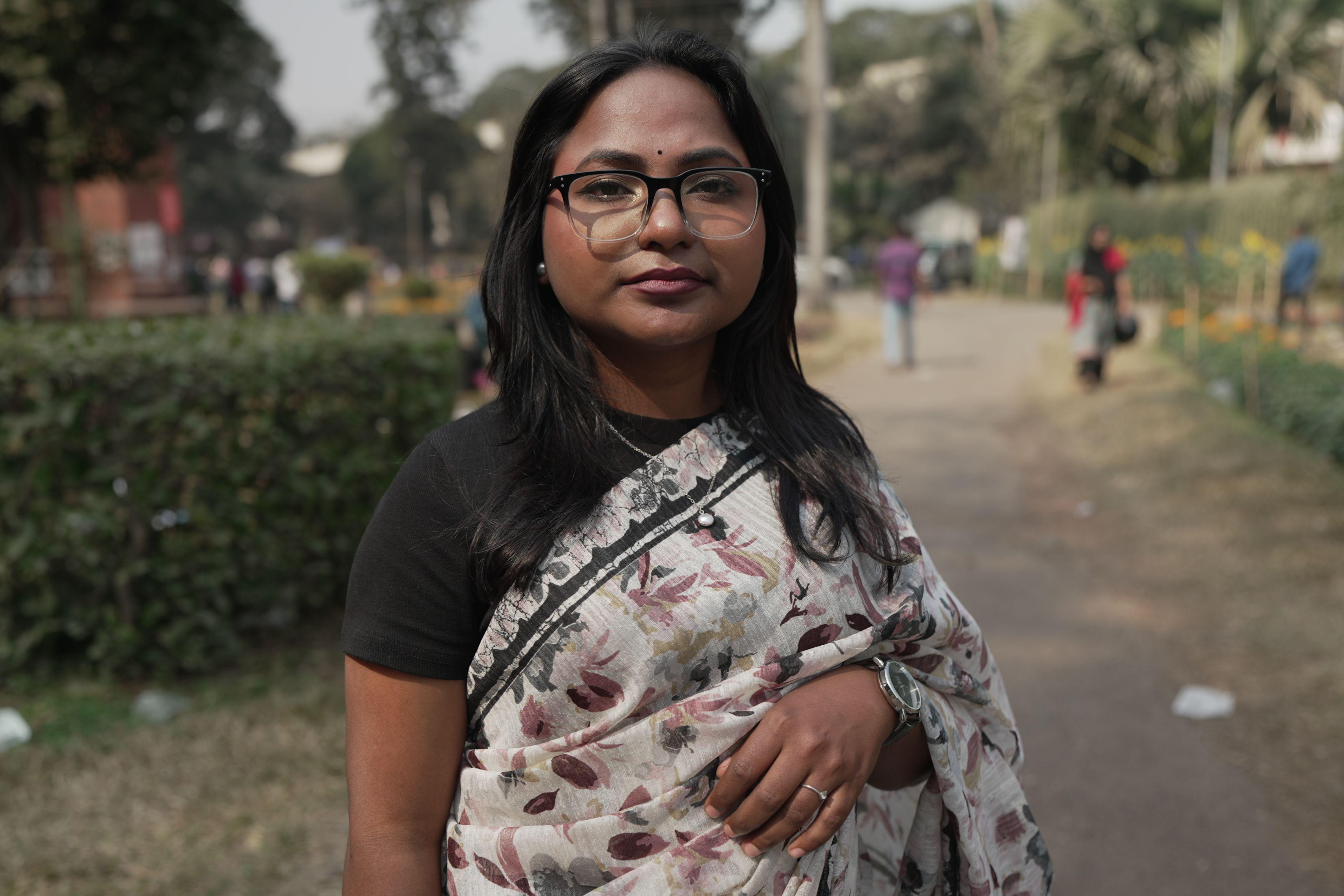 一名年輕女子，黑髮，戴眼鏡，身穿一件彩色紗麗長袍，內搭黑色上衣。