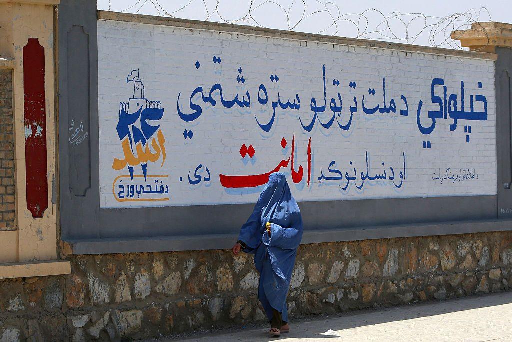 امرأة أفغانية ترتدي البرقع تمر بجانب جدارية تحيي الذكرى الخامسة لعودة حركة طالبان إلى السلطة، في ولاية غزني الأفغانية، في 13 أغسطس/آب 2026.
