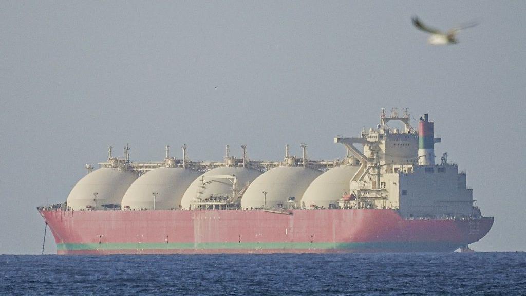 Un gigantesco buque cisterna rojo, con cinco enormes cúpulas blancas, se aleja de la cámara.